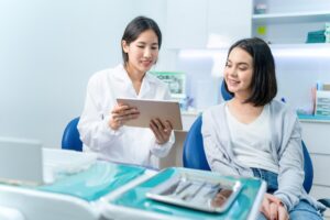 Asian dentist holding digital tablet and giving advice to Caucasian young girl patient.